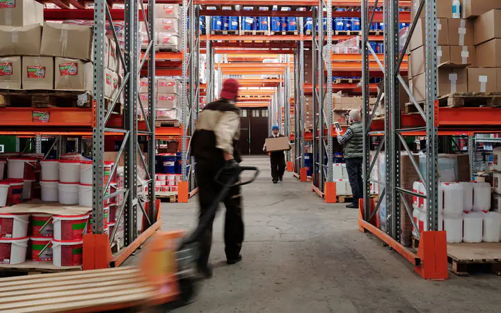 Pasillo de un depósito con estanterías cargadas de mercadería y un operario moviendo un pallet
